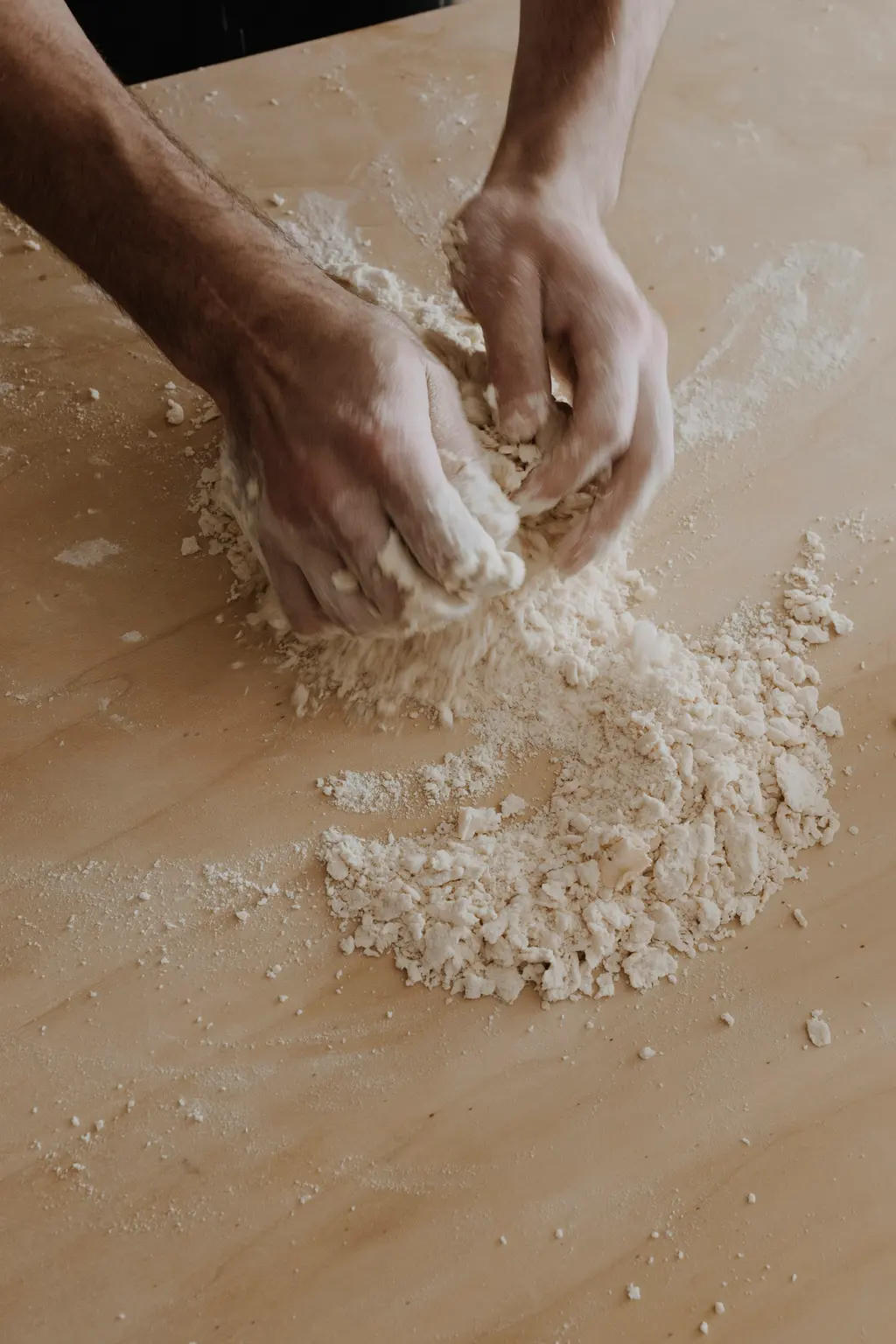 Manos enharinadas trabajando la masa sobre la mesa de madera del obrador